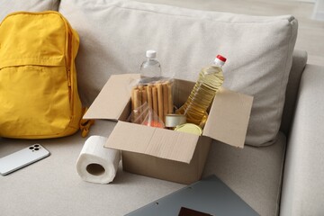 Survival kit. Different emergency supplies and food products in box on sofa