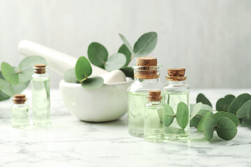 Bottles of essential oil, eucalyptus leaves, mortar and pestle on white marble table