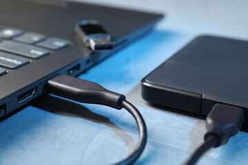 Hard disk drive with USB cable connected to laptop on blue textured table, closeup