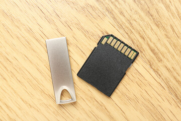 Flash drive and SD memory card on wooden background, flat lay