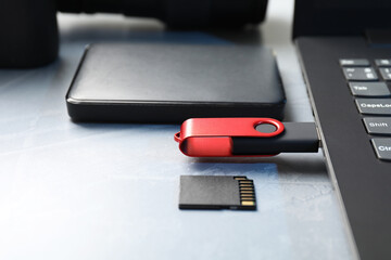 Flash drive connected to laptop, SD memory card and external hard disk on gray table, closeup