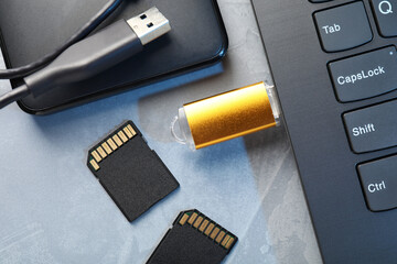 Flash drive connected to laptop, SD memory cards and external hard disk on gray textured table,...