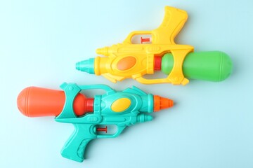 Bright plastic water guns on light blue background, top view