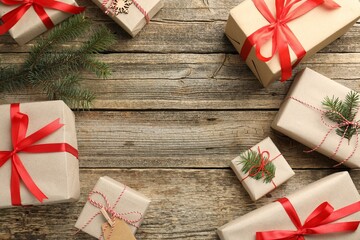 Frame of gifts wrapped in kraft paper with fir tree branches on wooden background, flat lay. Space for text