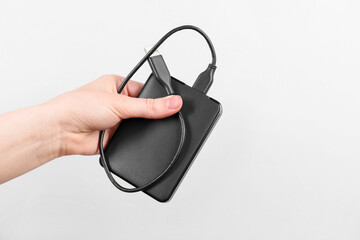 Man holding external hard drive with USB cable on light grey background, closeup. Space for text