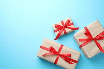 Fototapeta premium Many gifts wrapped in kraft paper with bow on light blue background, flat lay. Space for text