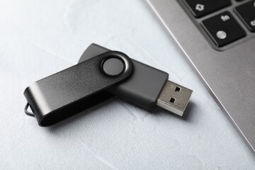Flash drive and laptop on light grey table, closeup