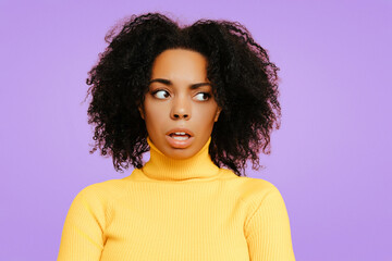 Surprised African American woman with natural curly hair, wearing a yellow turtleneck sweater, looking to the side with a shocked, confused expression against a soft purple background..