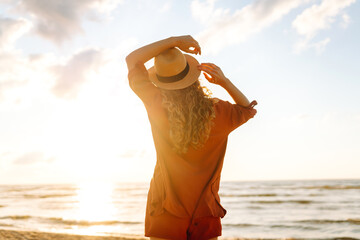 Back view of a young woman with curly hair feels free on the seashore. Young woman walks on the...