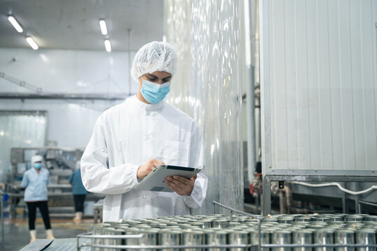 Industrial worker using digital tablet inspecting food process for production quality control in the operation of canned fish machine. the manufacturing line of fish factory