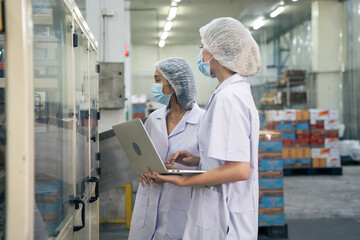 Industrial worker with colleague using laptop inspecting for production quality control in the operation of canned fish machine. the manufacturing line of fish factory