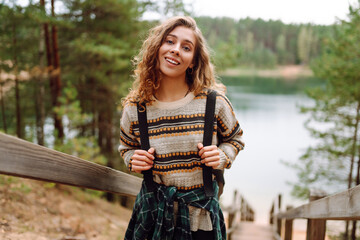 Young woman with backpack hiking on wooden paths in forest. Beautiful female traveler feeling freedom and enjoying lake view. Hiking, nature concept.