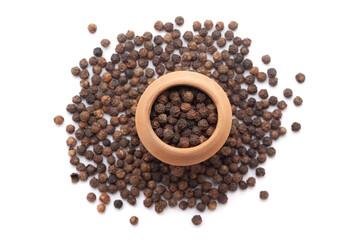 A mud pot filled with organic Black pepper (Piper nigrum) is placed on a heap of whole black pepper, isolated on a white background.