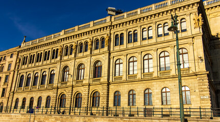 Facade of historic neoclassical building with arched windows and sculptures in Budapest, Hungary, illuminated by warm sunlight under clear blue sky