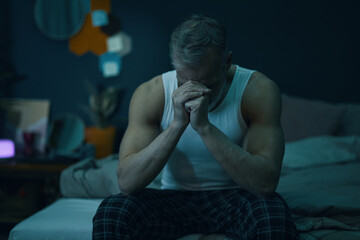 Middle-aged man sitting on a couch in a dimly lit room with his head in his hands, deep in thought....