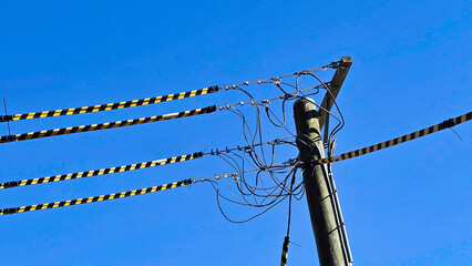Yellow and black striped synthetic tubes that (Tiger tails).Power lines connect to a utility pole against a bright blue sky in mid-afternoon
