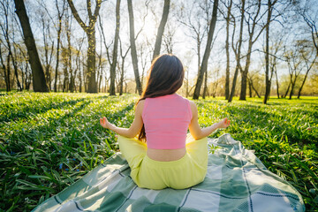 A young woman in a pink tank top meditates in a park