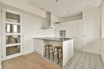 A stylish modern kitchen featuring sleek cabinetry, a spacious island with stools, and elegant flooring. The bright space emphasizes simplicity and functionality.