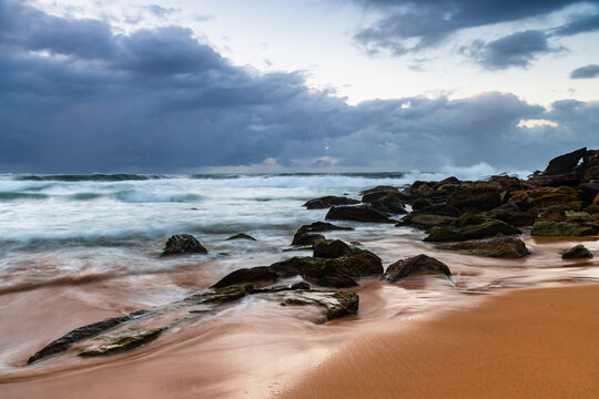 Sunrise at the seaside with rocks and rain clouds