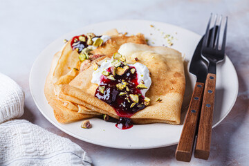 Breakfast crepes with sour cream, jam and pistachio.
