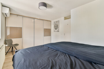A contemporary bedroom featuring minimalist furniture, a comfortable bed with a dark blue cover, and stylish decor that combines functionality with aesthetic appeal.