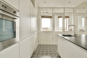 A sleek, modern kitchen featuring white cabinetry, large windows for natural light, and elegant patterned flooring. Ideal for contemporary home aesthetics.