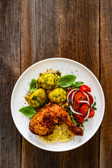 Baked chicken leg with boiled potatoes and fresh tomato salad on wooden table	