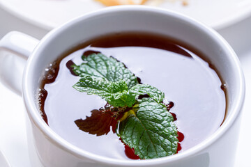 A cup of tea with a sprig of mint, close-up. A white cup with a thirst-quenching drink.