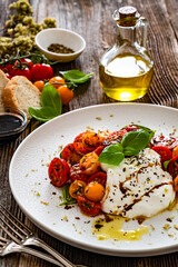 Caprese salad -  cherry tomatoes, fresh basil leaves and burrata cheese on wooden background