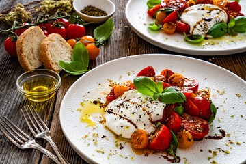 Caprese salad -  cherry tomatoes, fresh basil leaves and burrata cheese on wooden background