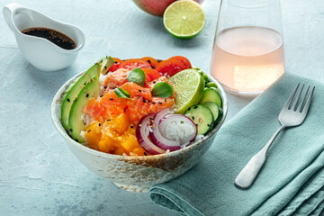 Poke bowl with salmon. Hawaiian salad with rice, fish, tomato, and avocado. Healthy diet. Shot on a table, with a drink and soy sauce