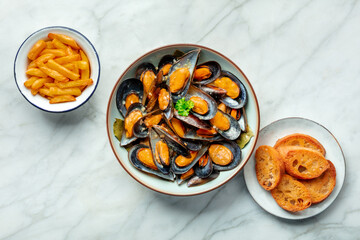 Mussels with French fries and toasted bread, moules frites, overhead flat lay shot on a marble background, seafood appetizer