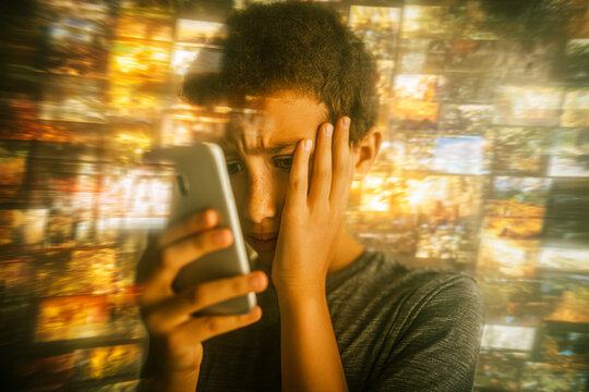 Boy with worried expression looks at phone, hand on face, against blurred background of many images, suggesting information overload or digital stress