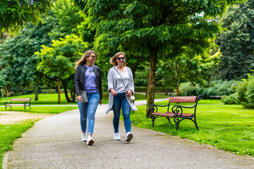 Two happy mature women walking in city park. Meeting of friends. Walk in park