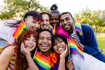 Happy multiethnic friends celebrating gay pride holding rainbow flags at park