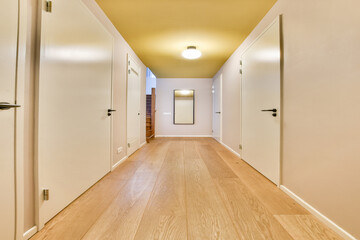 A spacious hallway featuring clean lines, light wood flooring, and neutral walls, leading to a staircase and illuminated by a central light fixture.