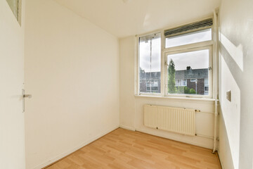 Empty minimalist room featuring a large window, light-colored walls, and wooden floor, offering a sense of openness and potential for decorating.