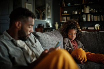 Father and daughter sit on sofa, girl looking upset, father on phone, depicting family disconnect and communication issues
