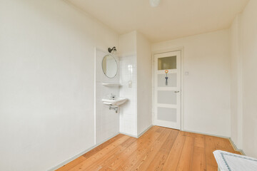 A well-lit, minimalist interior space featuring light-colored walls, a small sink, and wooden flooring, evoking a sense of simplicity and calmness.