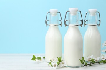 Fresh milk and blossoms on white table against light blue background. Space for text