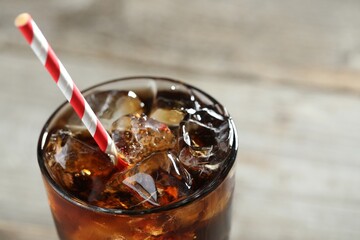 Refreshing cola with ice cubes and straw in glass on blurred light background, closeup. Space for text