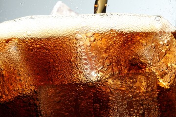 Pouring refreshing cola into glass with ice cubes against light grey background, macro view