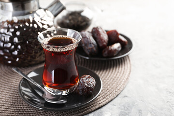 Traditional Turkish tea in glass cup, teapot and dates on light grey table, closeup. Space for text