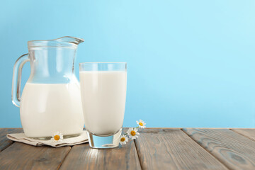 Fresh milk and flowers on wooden table against light blue background, closeup. Space for text