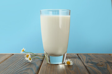 Fresh milk in glass and flowers on wooden table against light blue background, closeup