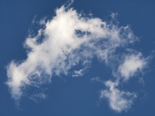 Large white cloud with soft, wispy tendrils and an irregular shape stretching across a deep blue sky, creating a dynamic and airy natural background