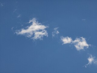 Two main wispy cloud clusters with trailing strands dispersed across a clear blue sky, forming a serene and minimal atmospheric background