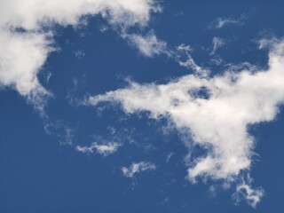 Light, wispy white clouds scattered across a vibrant blue sky, creating a natural and airy background with a peaceful and serene atmosphere