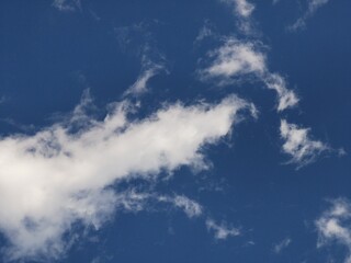 Long, narrow white cloud with feathery edges stretches diagonally across a deep blue sky, forming a tranquil and spacious natural background.