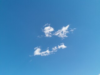 Two small, delicate wispy clouds float distantly in a vast, clear blue sky, forming a minimalist...
